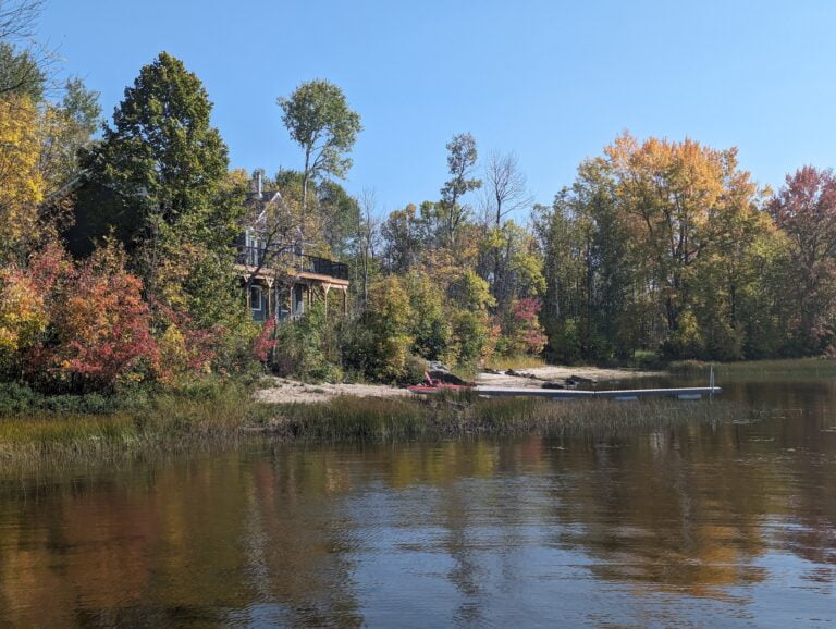 A charming lakeside cottage surrounded by autumn colors, with a sandy beach and dock leading to the lake.
