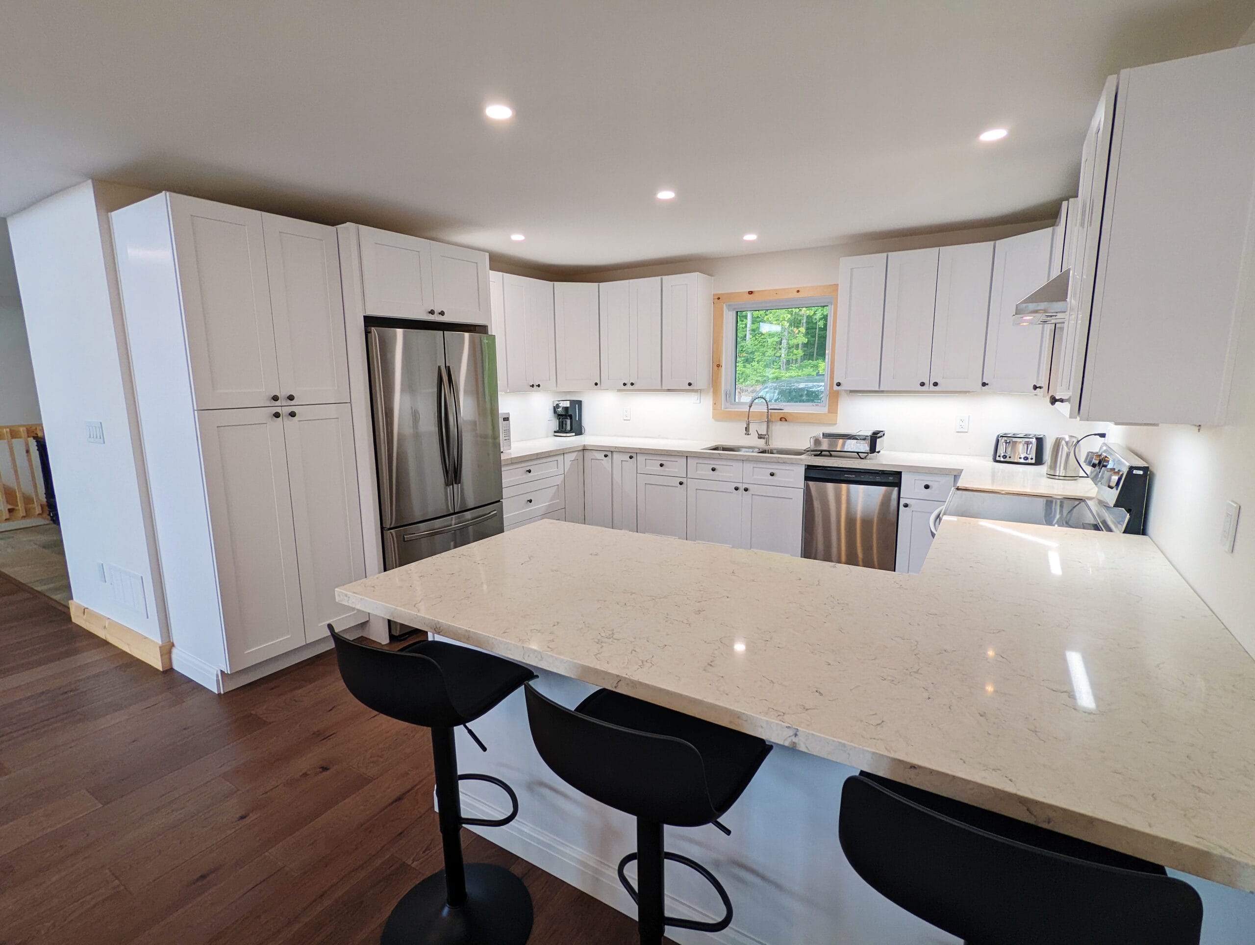 Bright, modern kitchen with quartz countertops and stainless steel appliances. Full-size fridge, ample white cabinetry, and a cozy breakfast bar with seating for two.