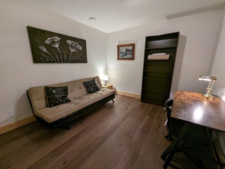 A quiet room with a foldable futon, ideal for lounging or sleeping. A small wooden desk and shelf provide a perfect setup for remote work or reading.